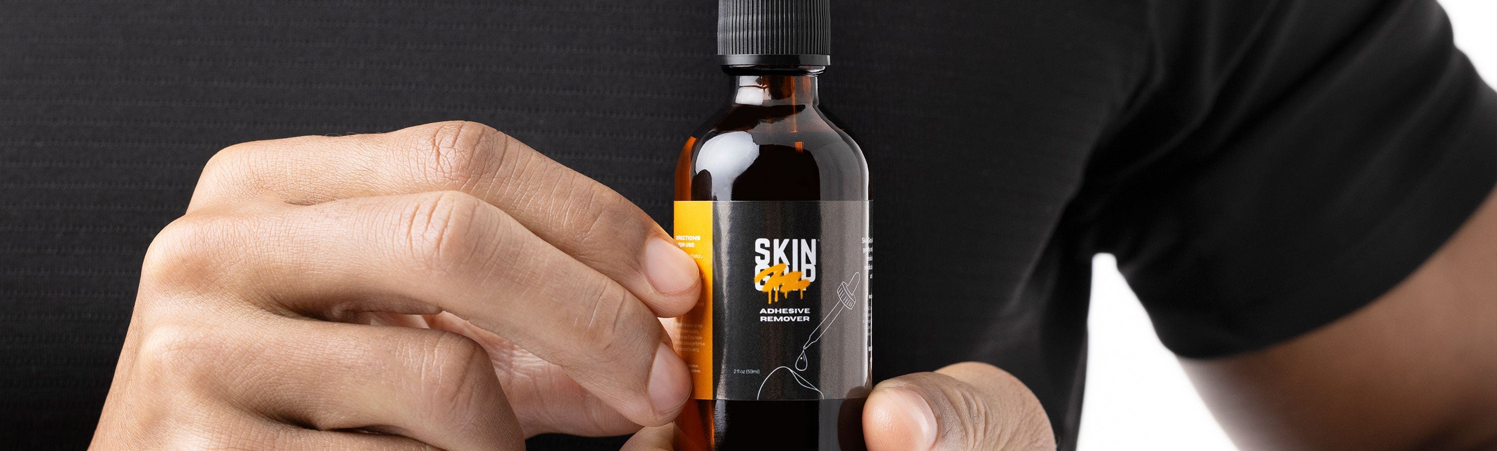 A person in a black t-shirt holding a Skin Grip amber glass dropper bottle with both hands, shown from the chest down against a dark background